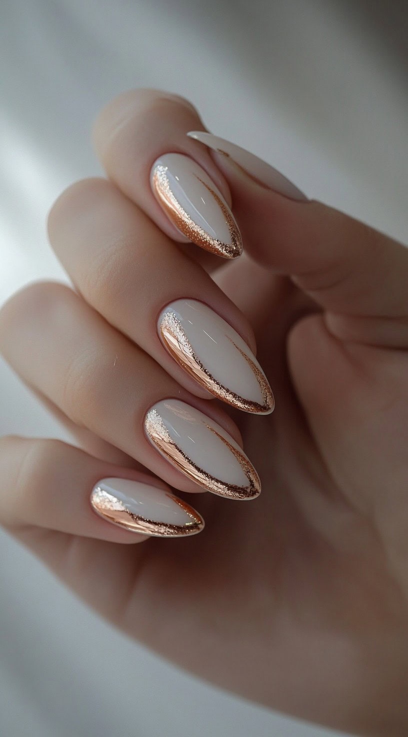 A close-up of a hand with almond-shaped nails featuring a glossy white base and rose gold metallic accents along the edges.