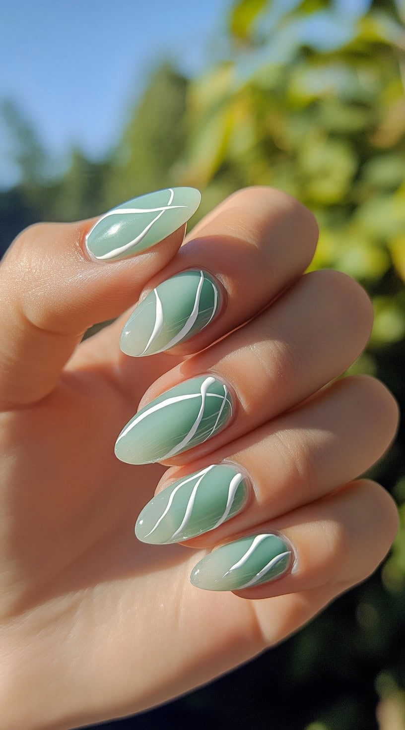Almond-shaped nails in a matte sage green shade with delicate white abstract line detailing.