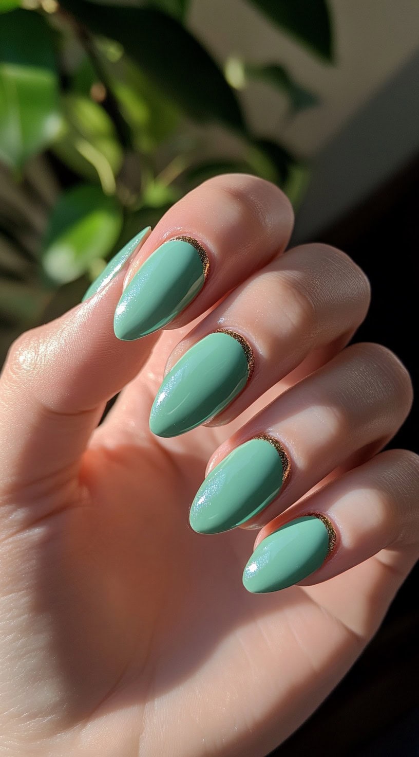 Soft sage green almond-shaped nails with delicate gold lining along the cuticles.