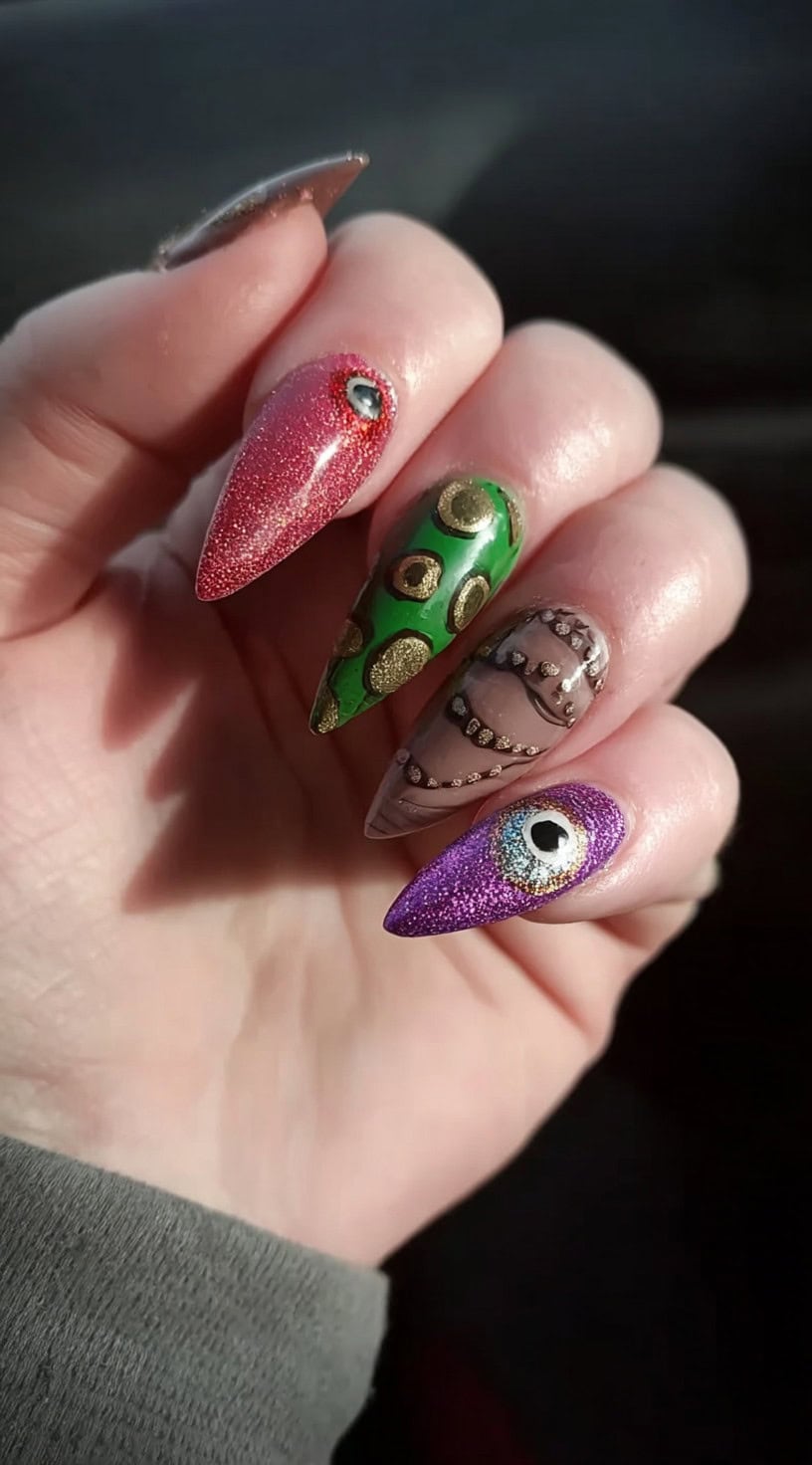 Pointed nails in glitter red, green, taupe, and purple, each embellished with raised eyes, tentacles, or stitched motifs.