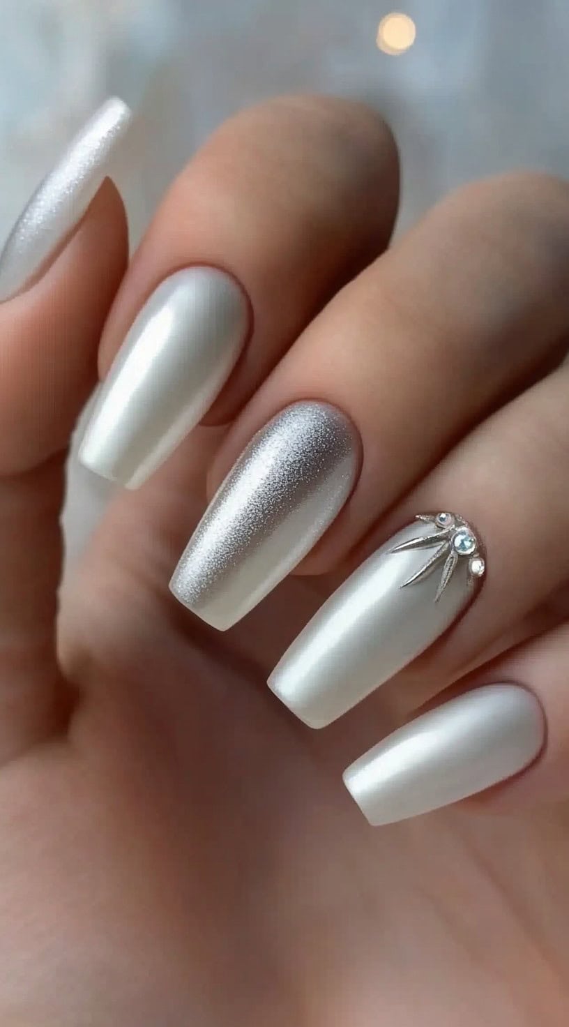 A close-up of long, coffin-shaped nails with a pearly satin finish, one accent nail featuring delicate rhinestones and metallic silver details.