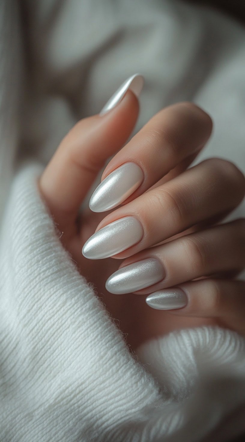 A close-up of almond-shaped nails featuring a soft pearlized white finish with a satin glow.