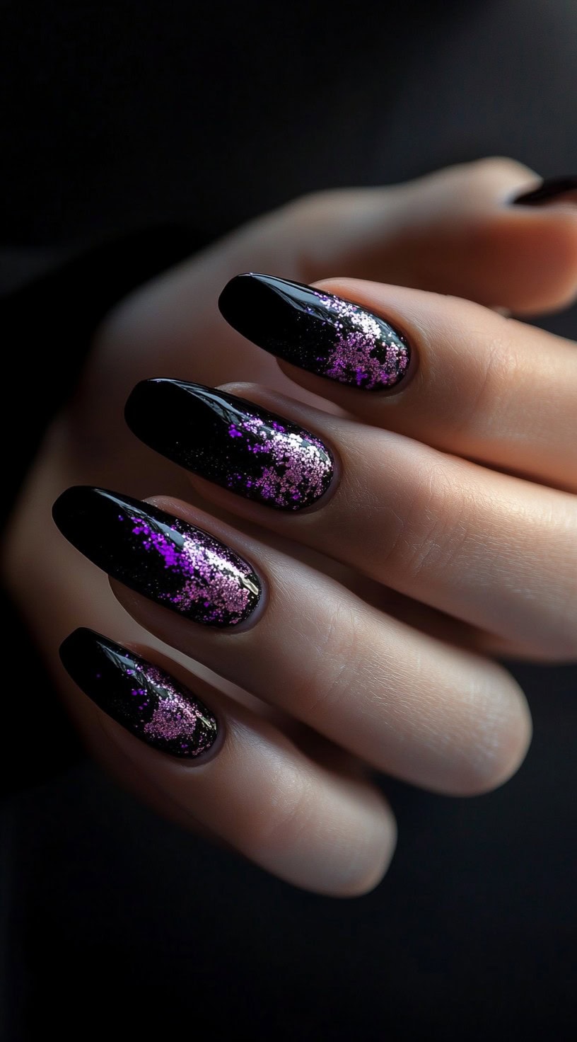 Oval-shaped nails painted black with scattered pink and purple glitter over the surface.