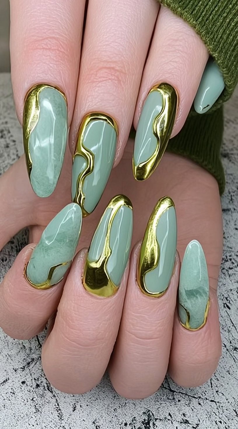 A hand with long almond nails painted in light jade, each outlined with dramatic dripped gold chrome borders.