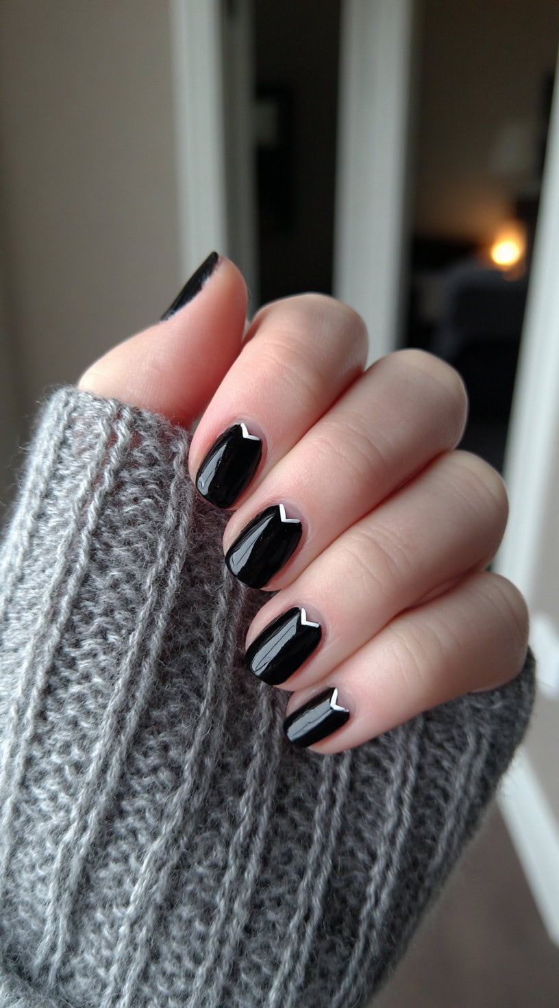A hand with short glossy black nails featuring a small inverted white chevron at the cuticle area of each nail.