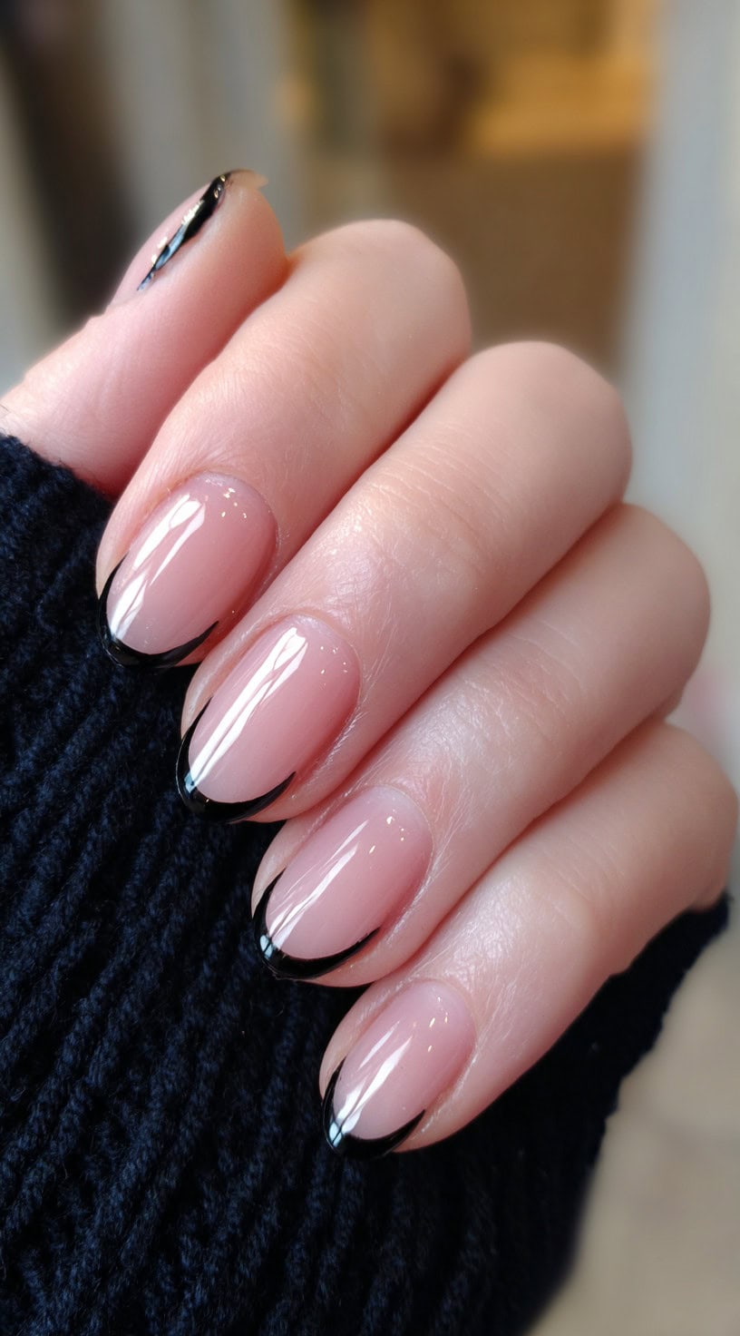A hand with short oval nude nails featuring curved black flame-like French tips.