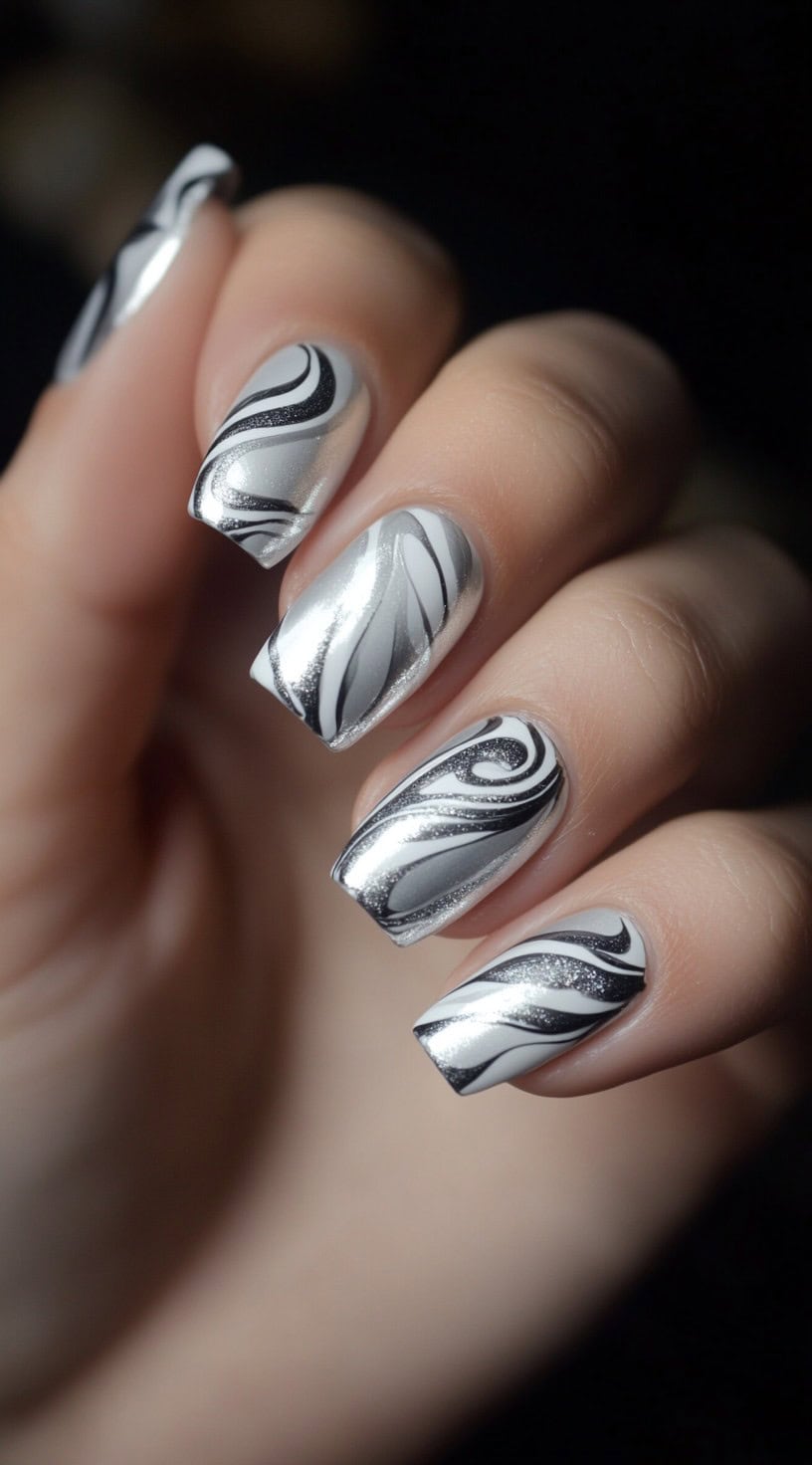 A close-up of square-shaped nails with a mix of silver, black, and white swirls creating a marble-like effect with a glossy finish.