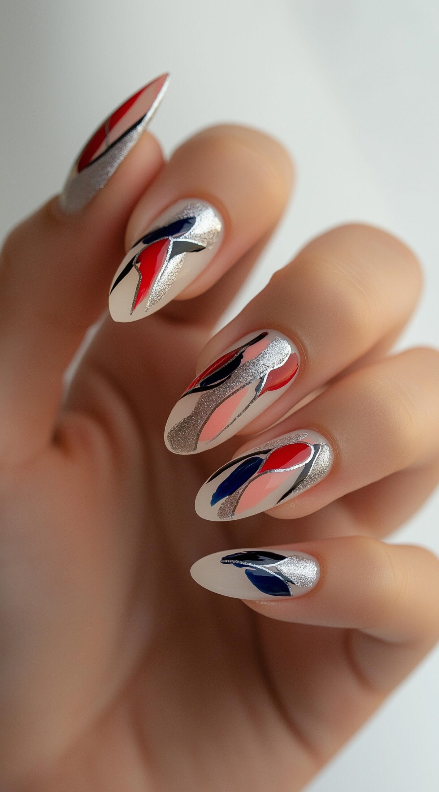 A hand with almond-shaped nails featuring bold abstract strokes in red, blue, and silver with a metallic shimmer.