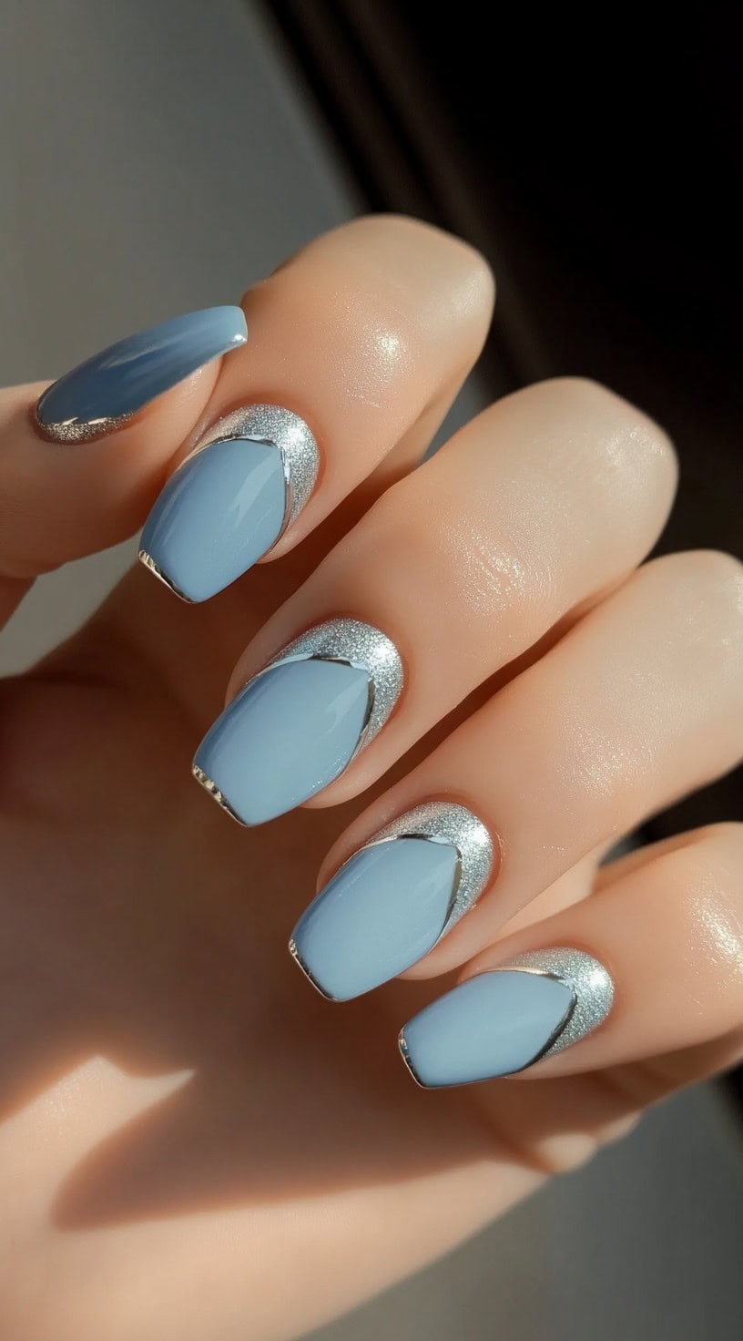 A close-up of a hand showcasing baby blue square nails with silver-glittered half-moon cuticle accents.