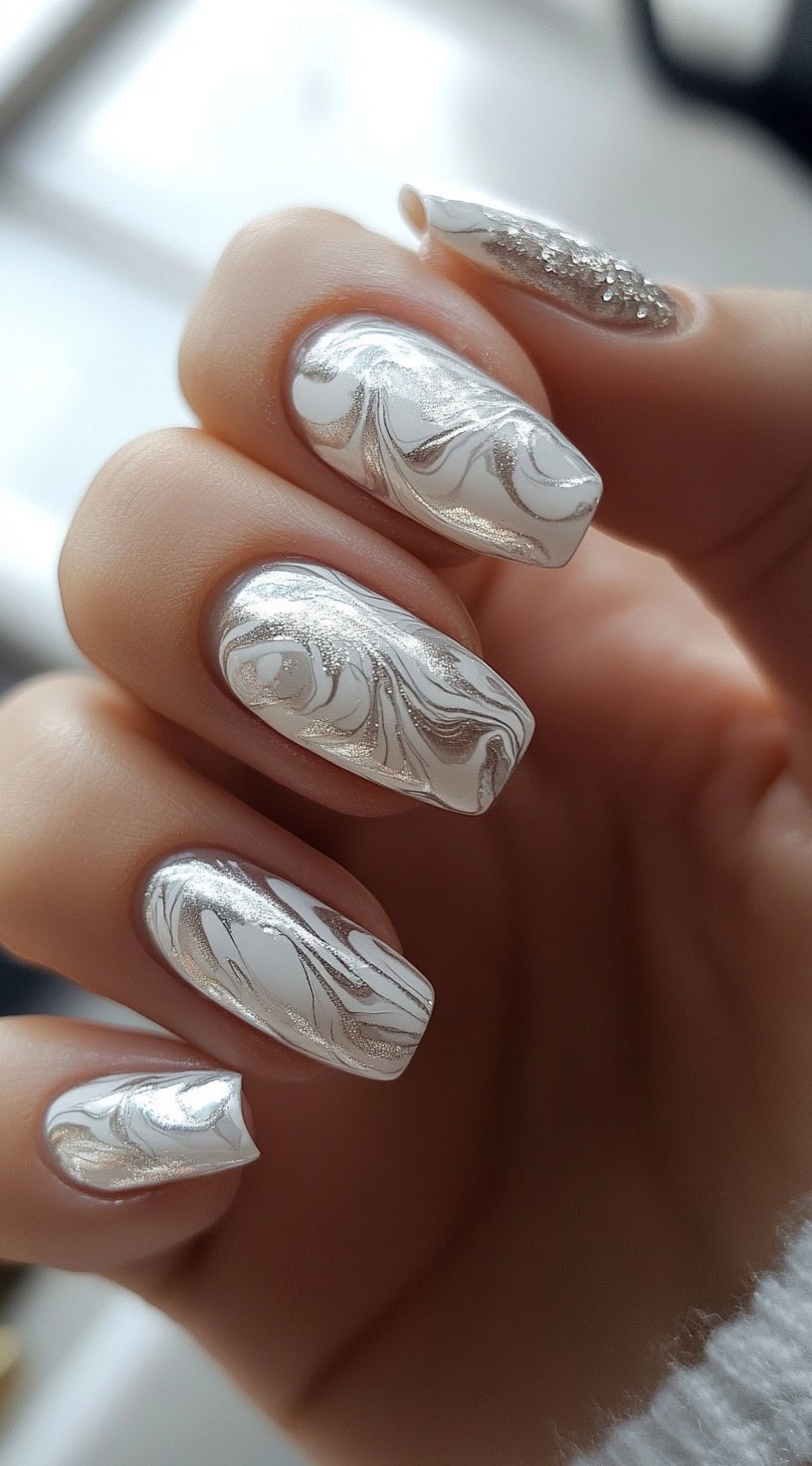 A close-up of silver and white marble-effect gel nails in a coffin shape, with subtle glitter details enhancing their luxurious and modern appearance.