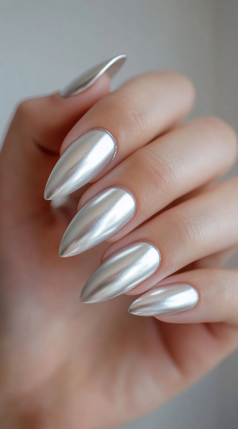 A close-up of almond-shaped nails painted in a smooth, high-shine metallic silver finish.