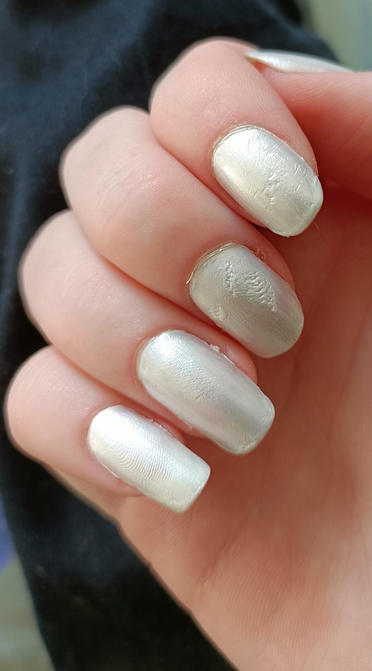 Close-up of metallic white nail polish with visible fingerprint smudges and uneven texture.