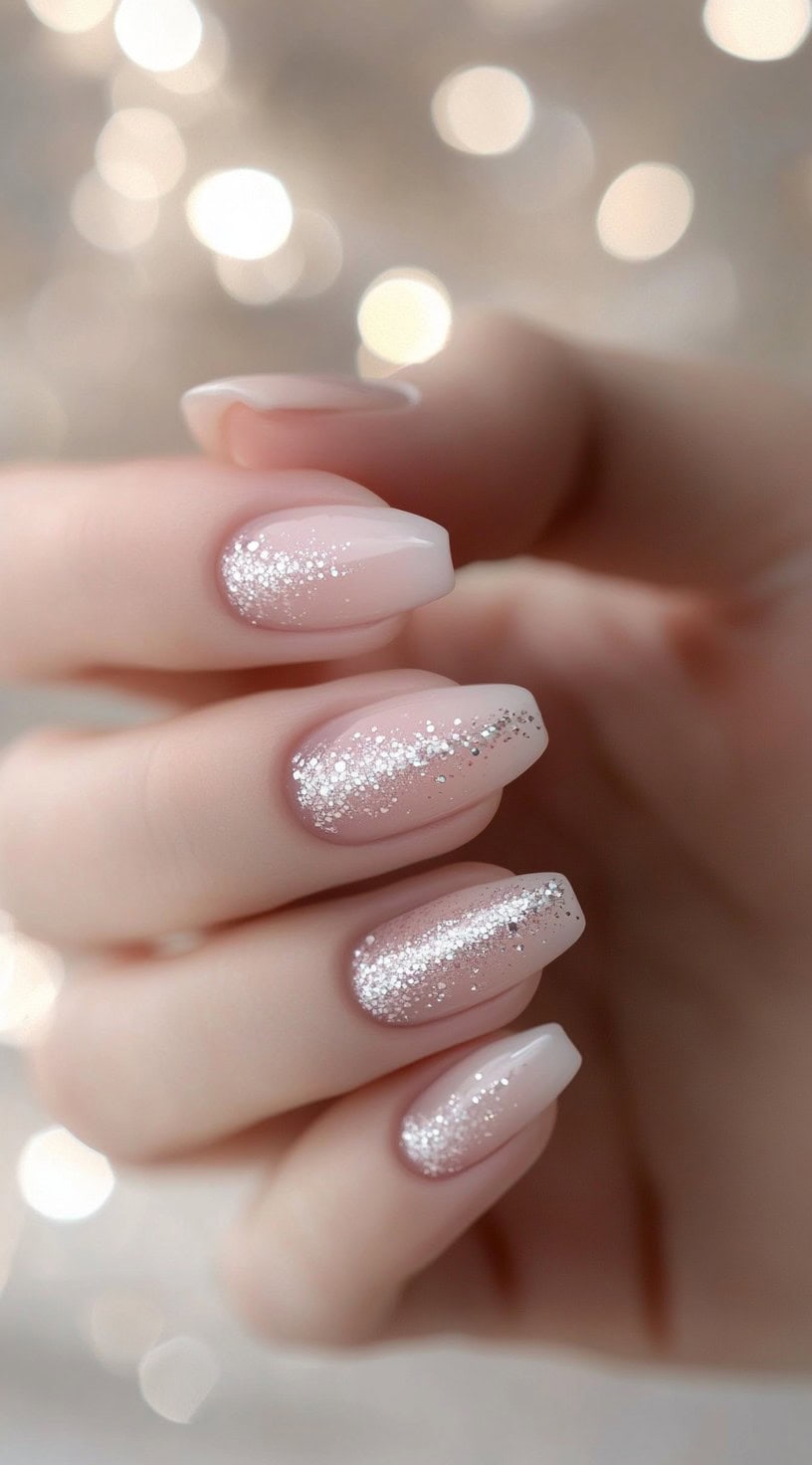 A close-up of almond-shaped nails with a soft nude-pink base and a cascading silver glitter gradient for a timeless and elegant bridal look.