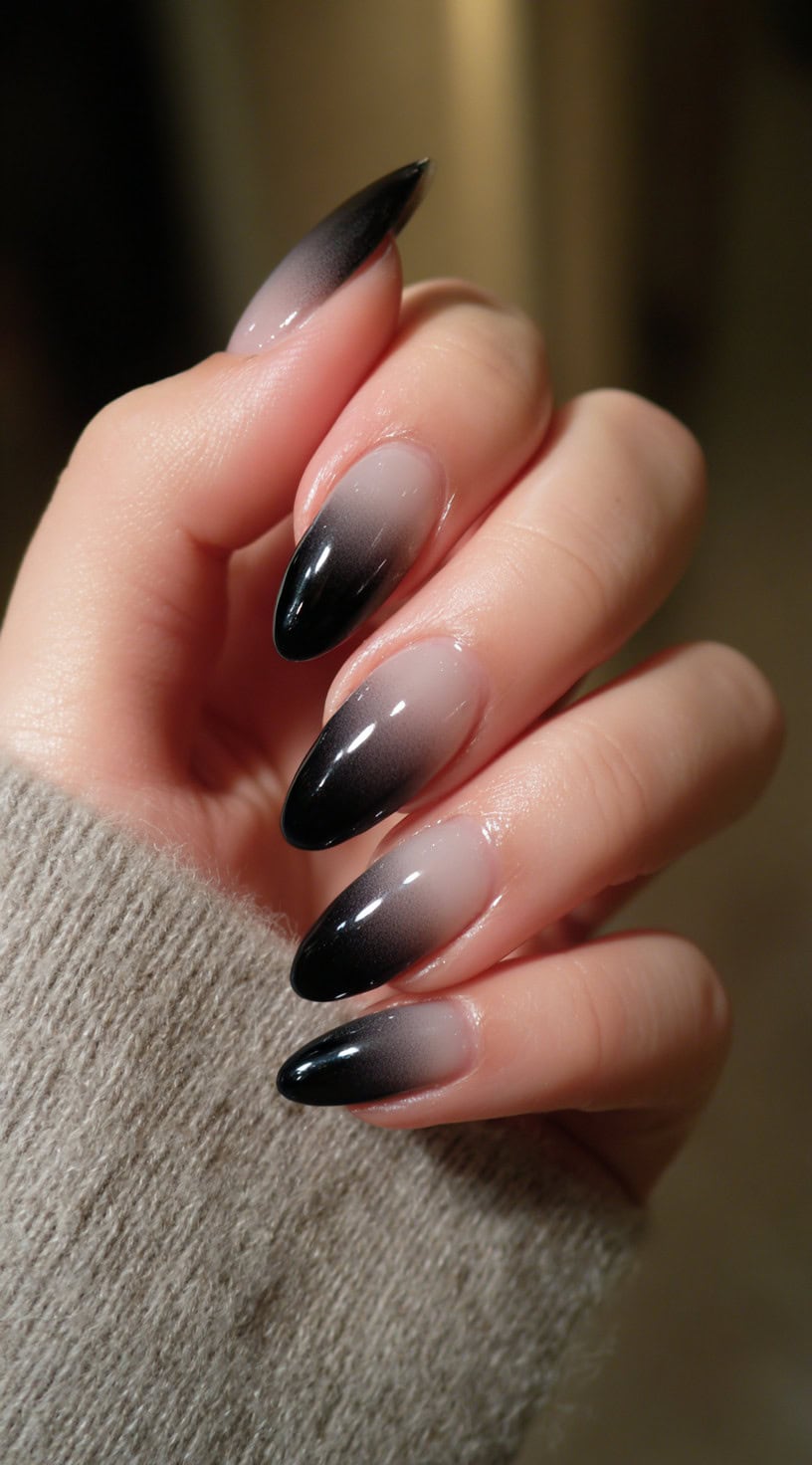 A hand with almond-shaped nails featuring a smooth nude-to-black ombre gradient.