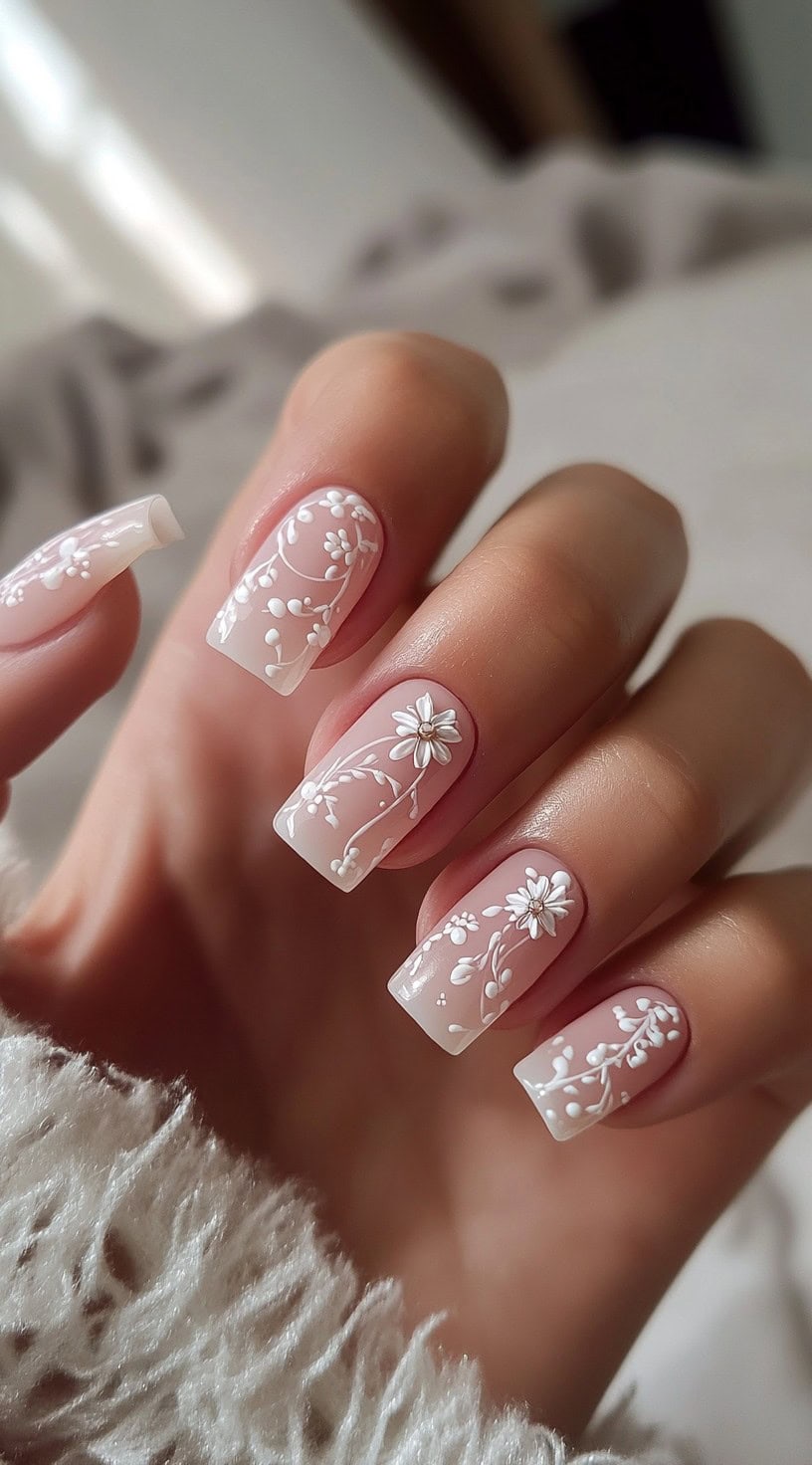 A set of square-shaped nails with a soft pink base and intricate white floral patterns.