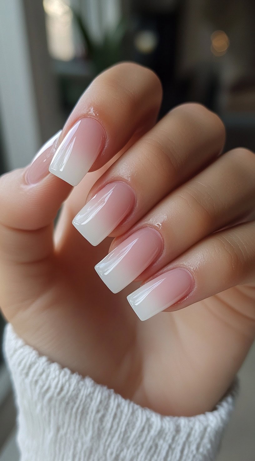Close-up of a hand with square-shaped nails featuring a soft baby pink to white ombre fade.