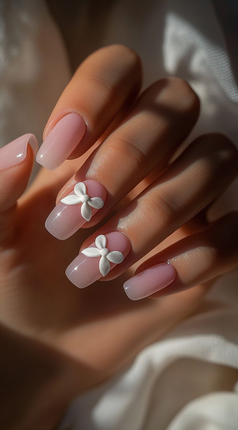 A set of square-shaped nails in a soft pink gradient, featuring delicate 3D satin bows on two fingers.