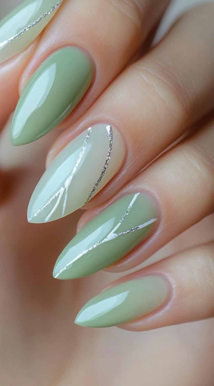 A set of almond-shaped nails in soft sage green and milky white hues, featuring delicate silver lines for an airy, sophisticated look.