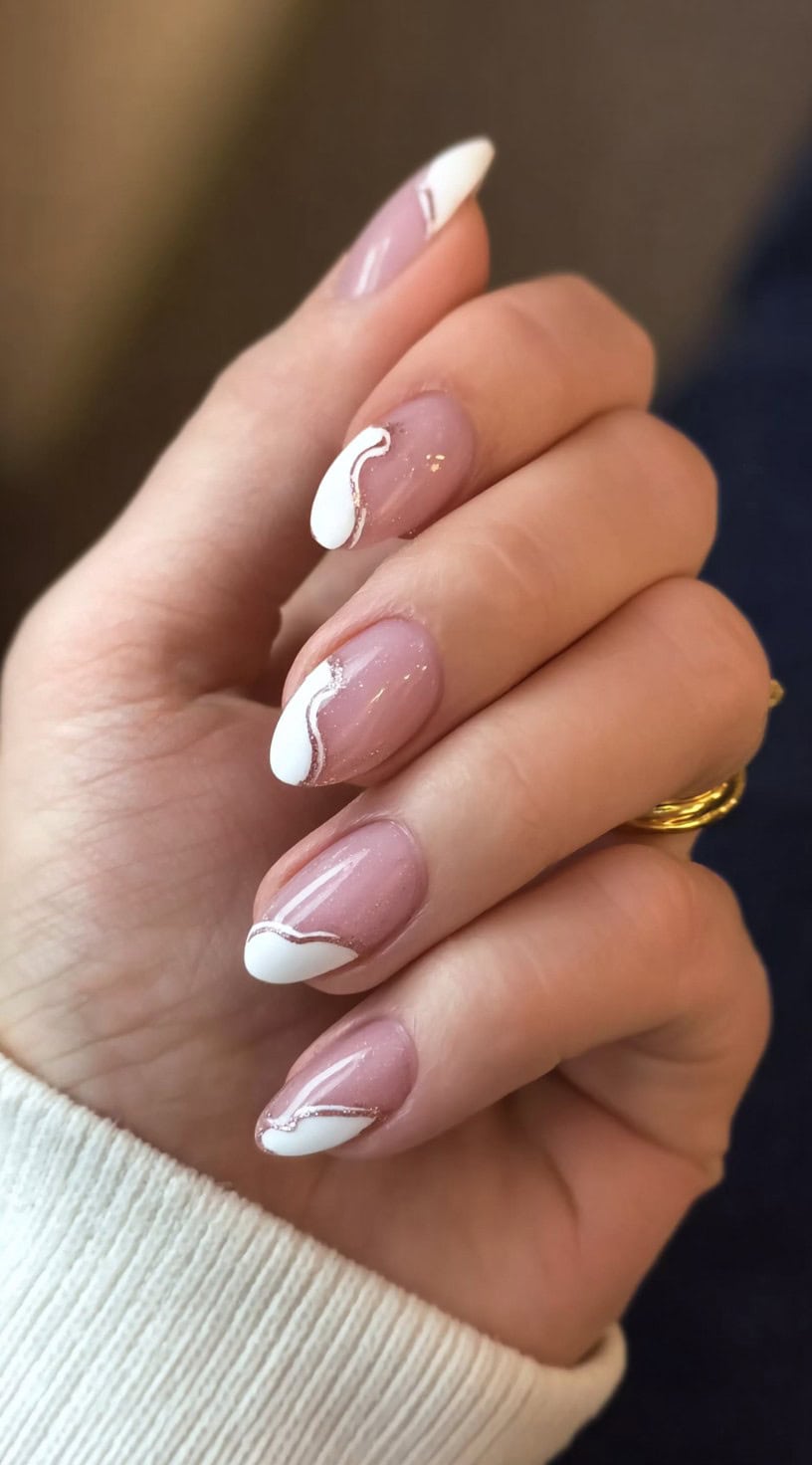 Short almond nails with a natural pink base and white wavy French tips outlined in fine silver glitter.