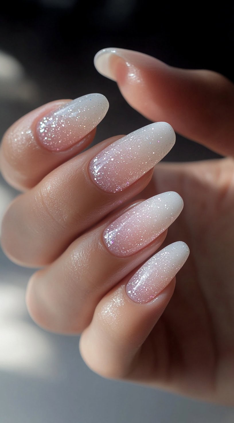Almond-shaped nails with a sheer pink-to-white ombre base, lightly dusted with fine white glitter for a dreamy effect.