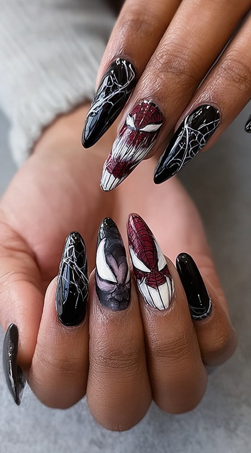 A hand with long almond nails featuring Spiderman and Venom face art along with black polish and white web detailing.