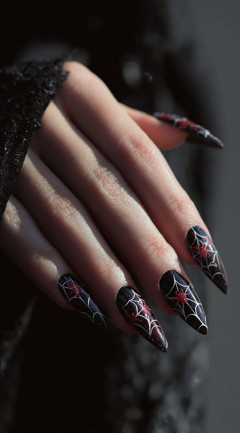 Almond-shaped black nails featuring white spiderwebs with small red spiders for a creepy-cute gothic look.