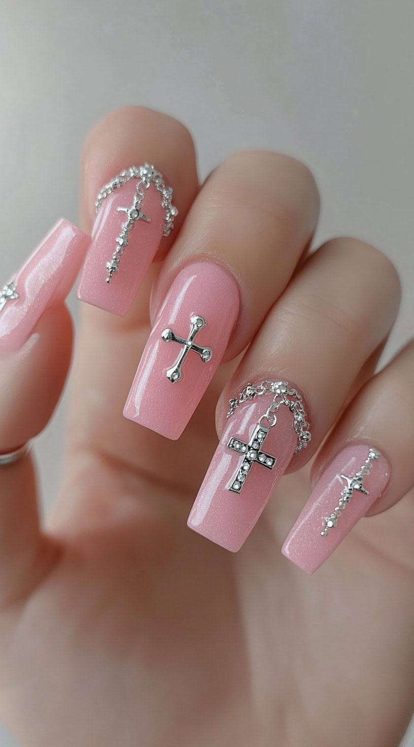 Pink square nails decorated with silver cross charms and silver chain accents.