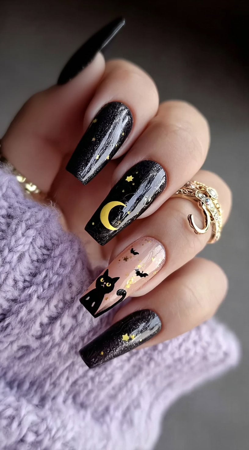 Long square nails with a mix of glossy black and nude bases, decorated with golden moons, stars, black cats, and tiny bats.