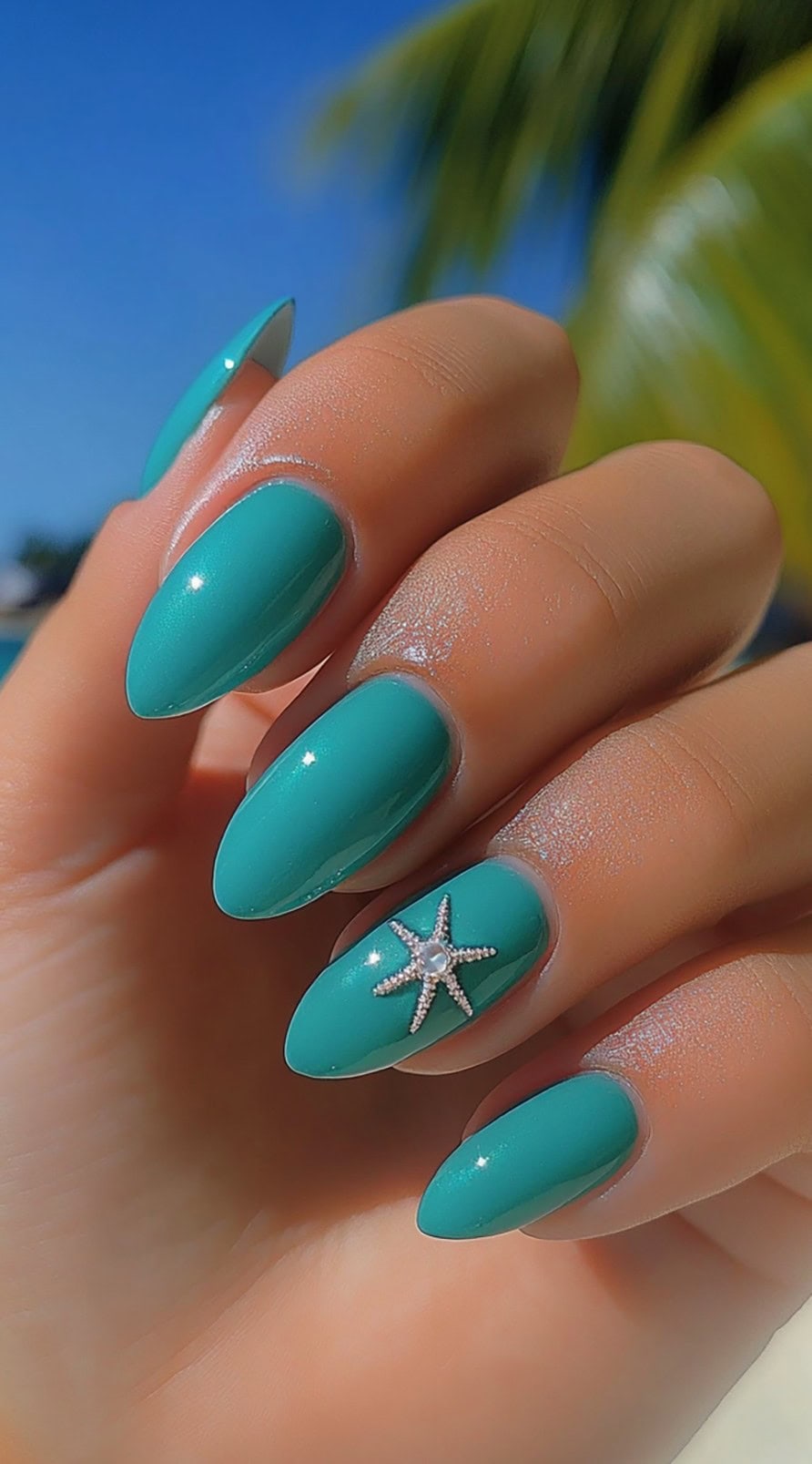 Glossy teal almond-shaped nails with a sparkling starfish charm on one accent nail, set against a tropical beach background.