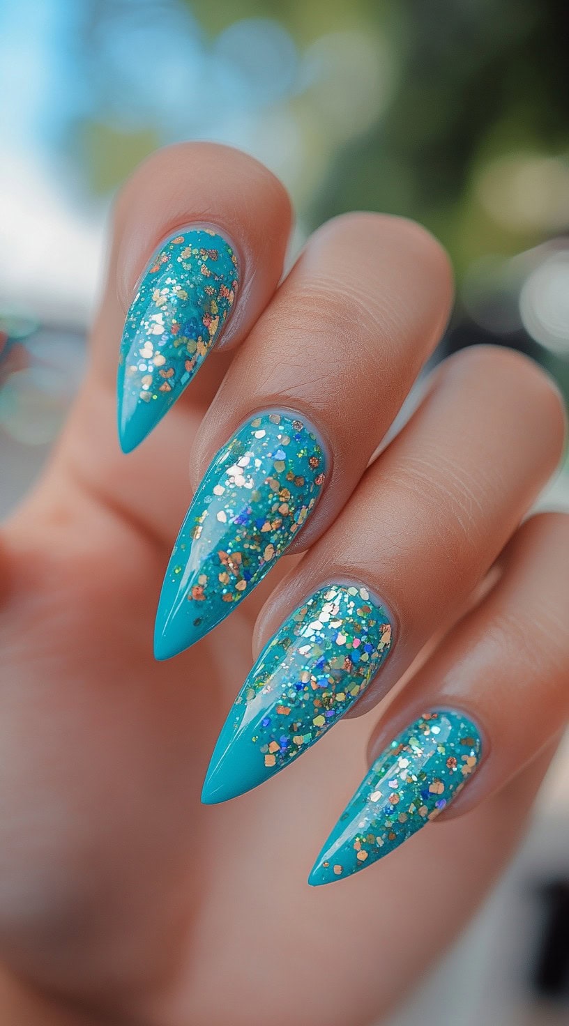 Bright turquoise stiletto nails covered in chunky iridescent glitter.