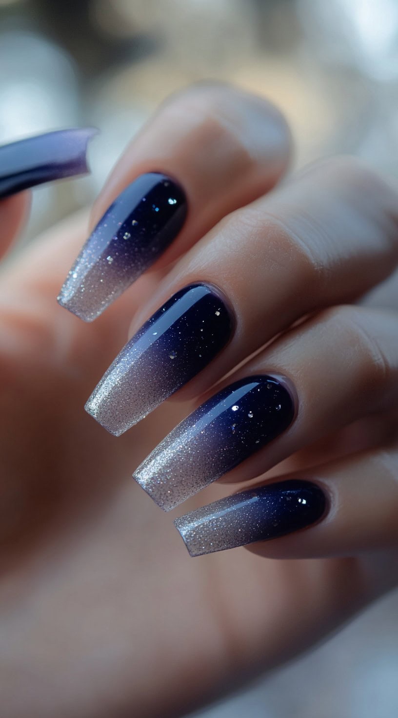 Coffin nails fading from deep navy to soft silver with scattered holographic glitter specks.