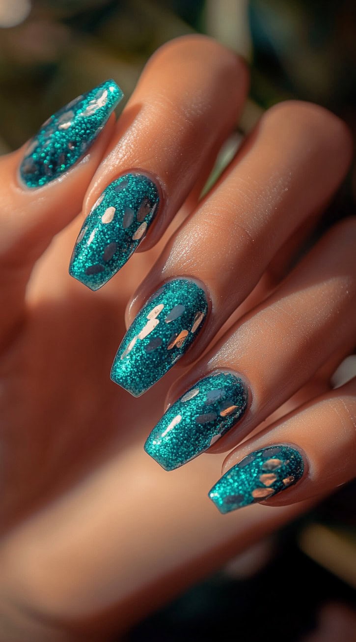 Vibrant aqua blue coffin nails covered in fine glitter with scattered gold foil accents.