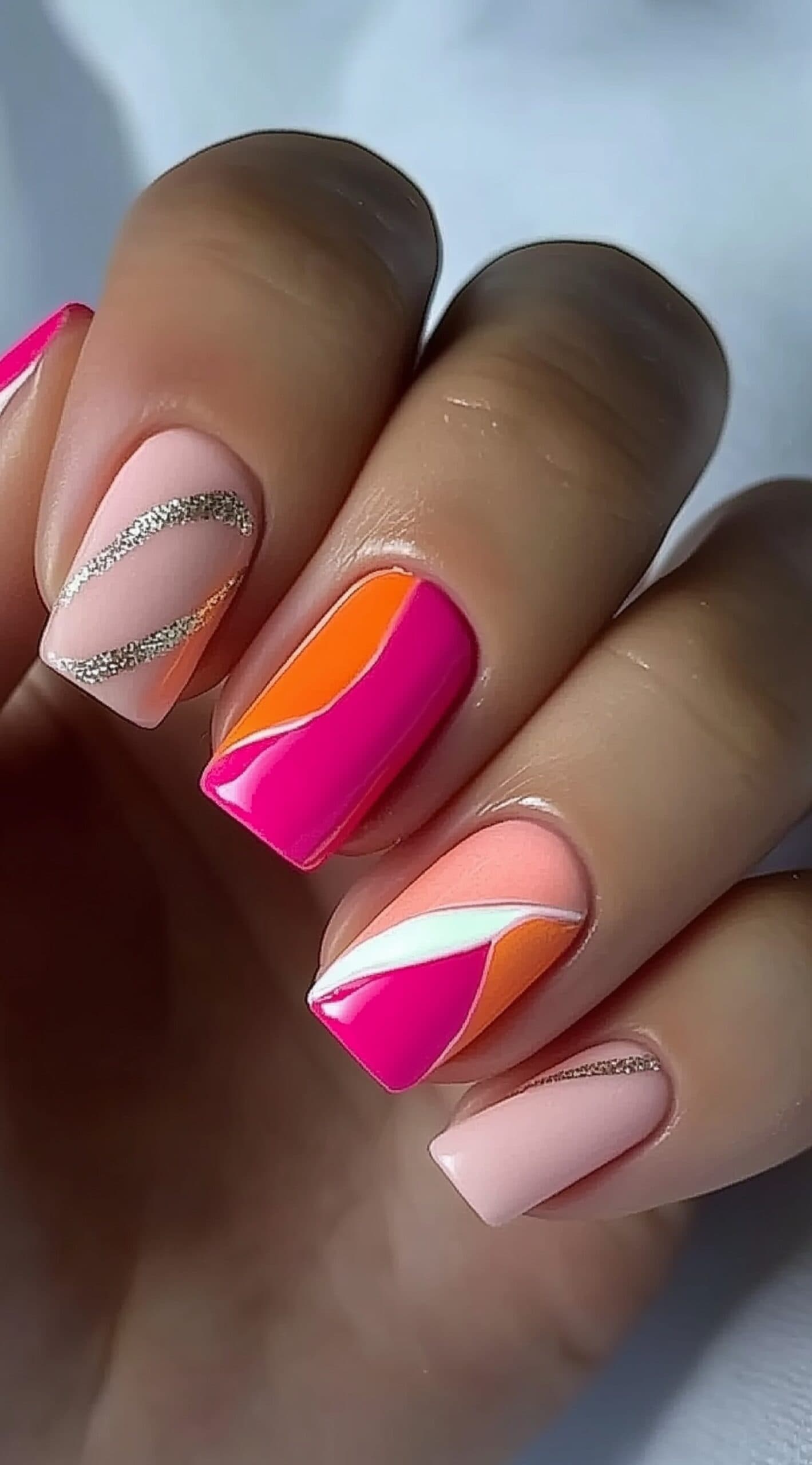 Bright square nails in pink, peach, and orange with abstract lines and glitter accents.