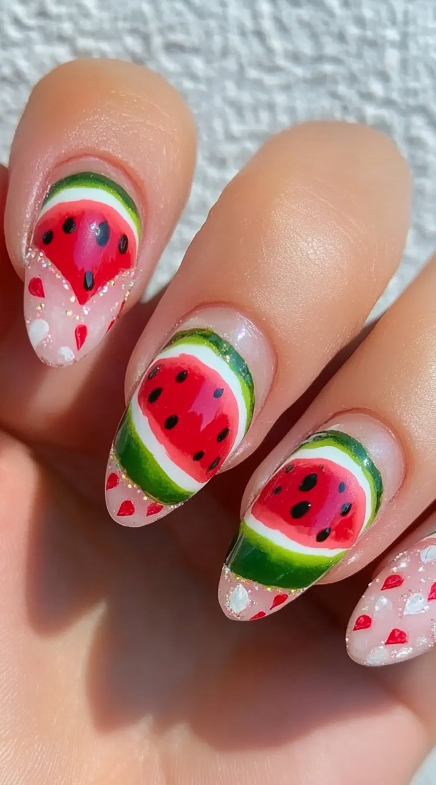 Almond nails decorated with vibrant watermelon slices placed along the lower half of each nail over a sheer base.