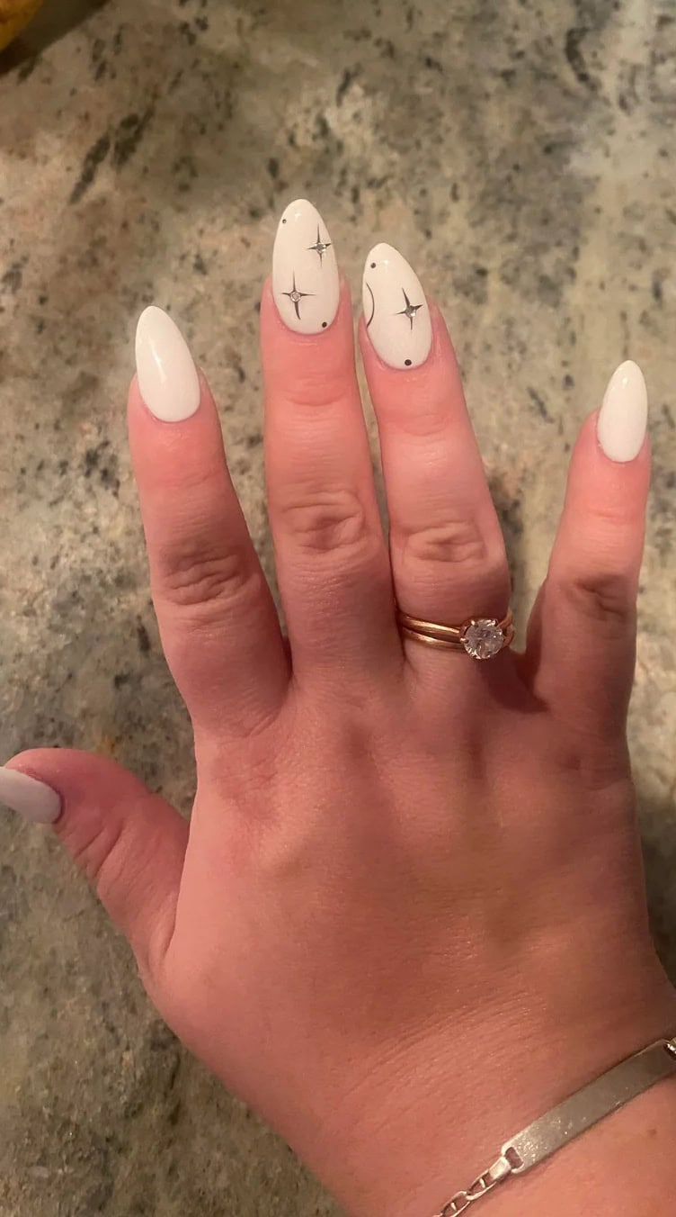 Long almond nails painted in creamy white with delicate silver star and dot accents for a soft, celestial look.