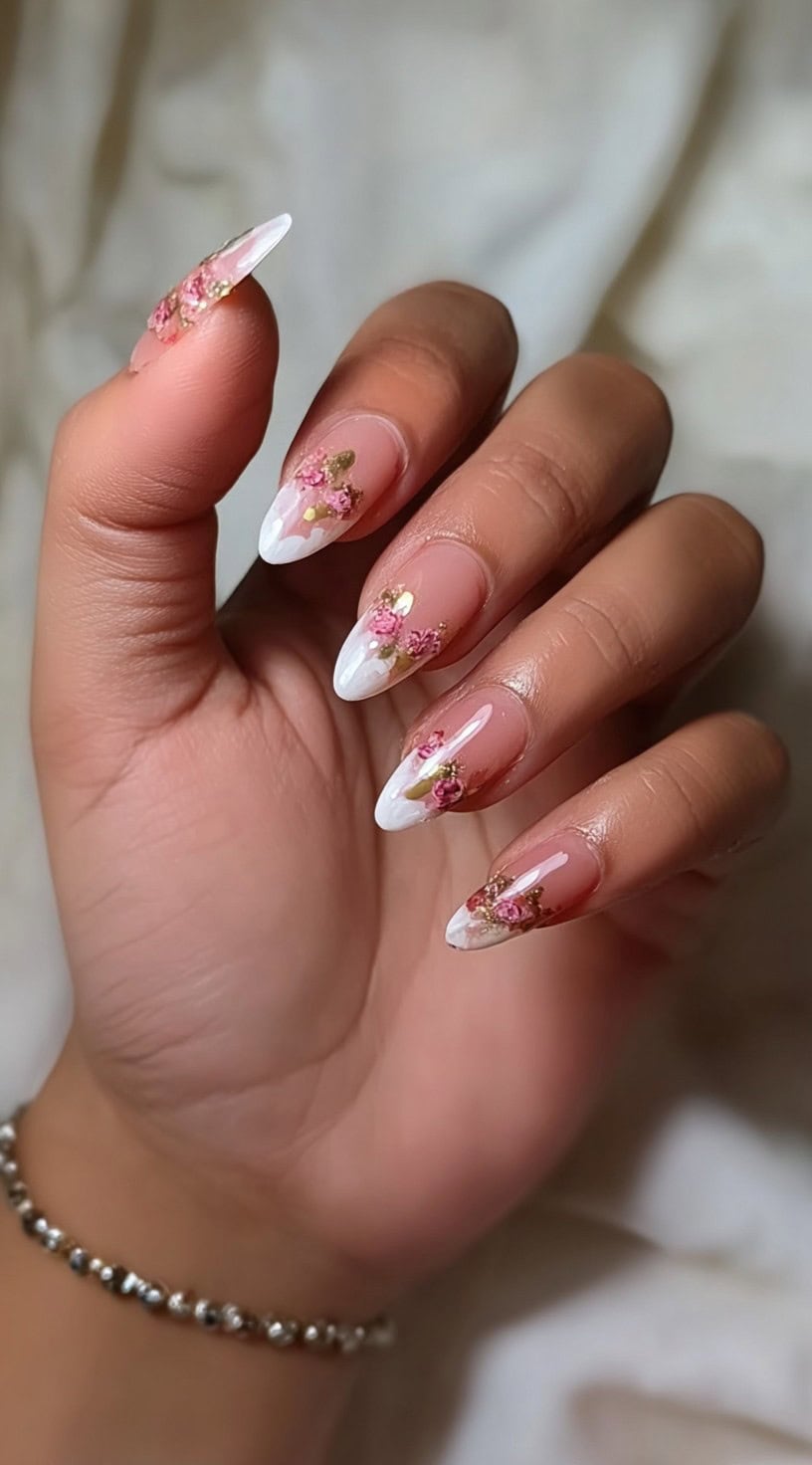 Almond nails with white sculpted tips decorated with small pink dried flowers and touches of gold leaf.