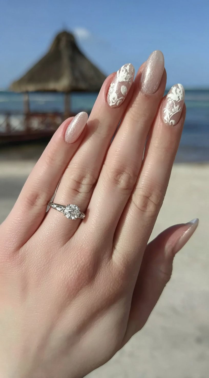 Almond nails with a soft nude shimmer base, enhanced with white 3D lace designs on accent fingers.