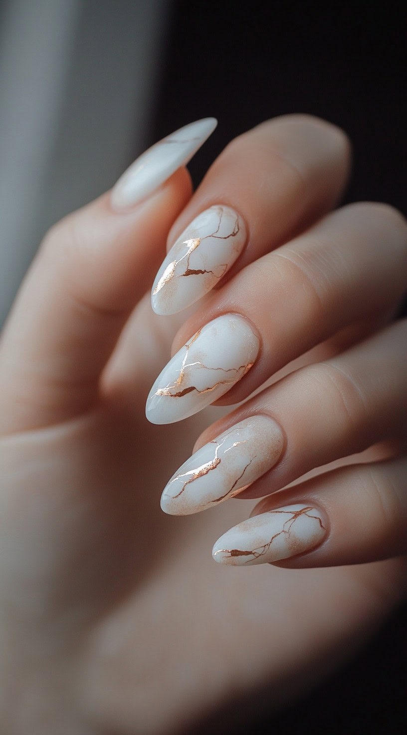 Five almond-shaped nails designed with a white marble effect, traced with thin, glimmering rose gold cracks.