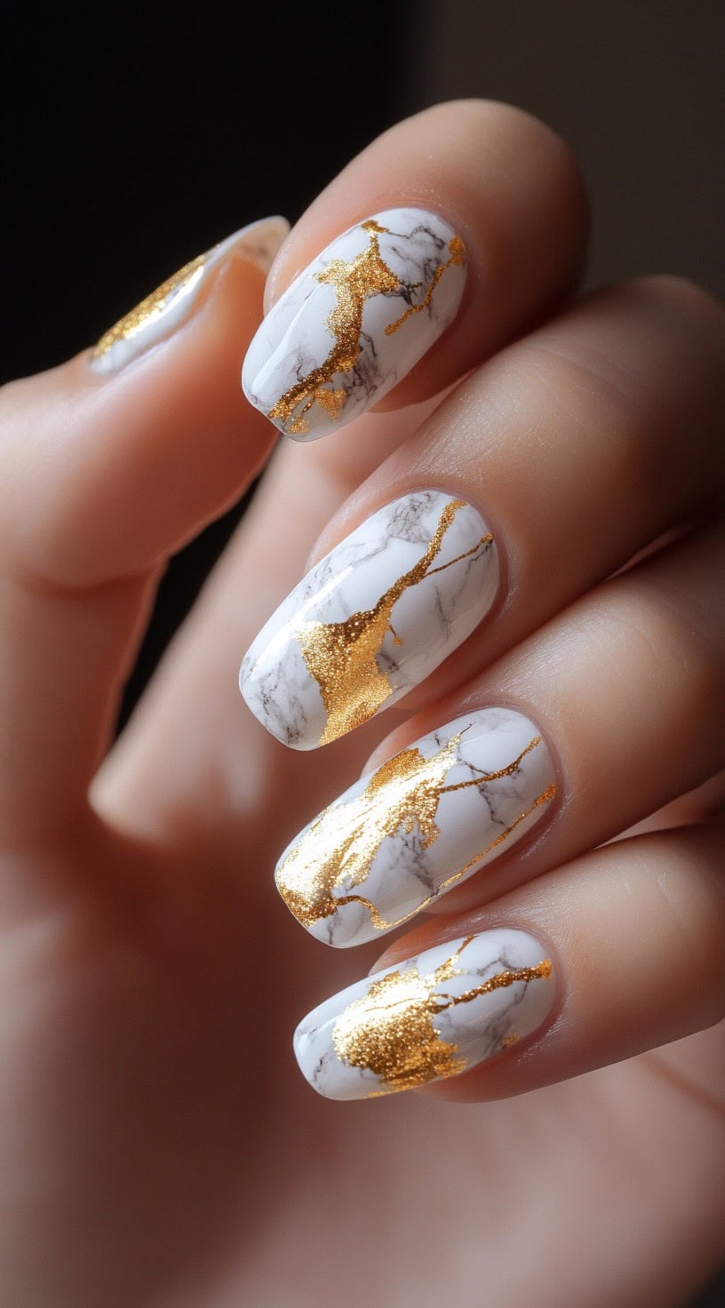 Medium-length, rounded nails with a white marble effect and irregular gold foil cracks, giving a sophisticated and artistic touch.