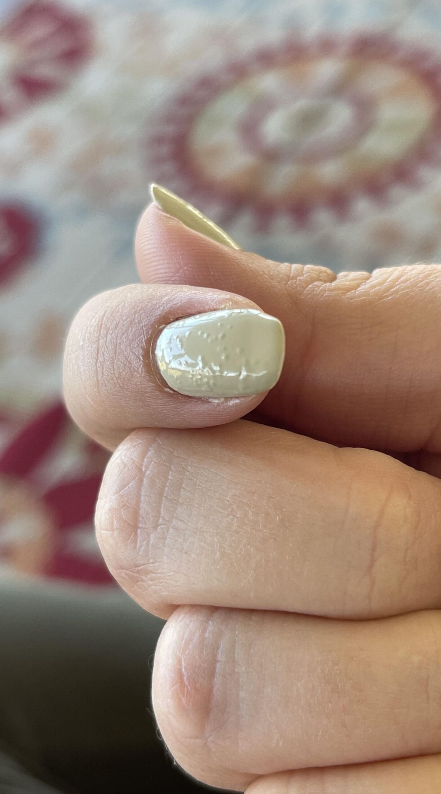 Thumb with glossy off-white nail polish showing small bumps and patchy bubbling, creating a flawed finish.